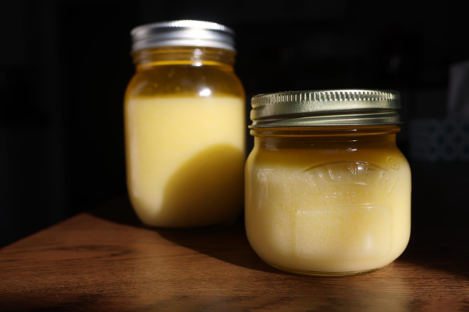 Two jars of our golden ghee catching the sunlight on a wooden table.